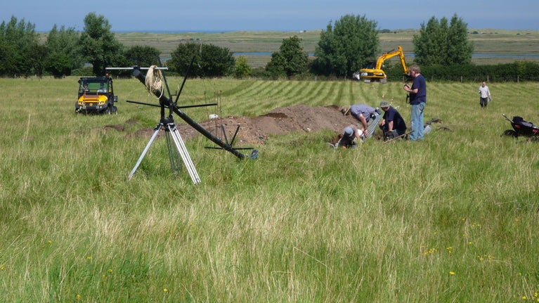 Archaeologists and volunteers working in a trench on the field at Brandounum that was dug as part of the last Time Team visit in 2012, with the coastline visible in the distance.